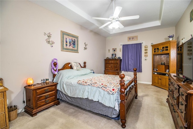 bedroom featuring a raised ceiling, light carpet, and ceiling fan