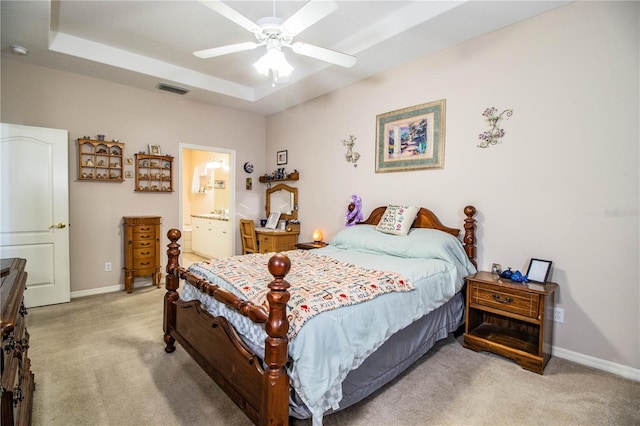 bedroom featuring connected bathroom, a tray ceiling, light colored carpet, and ceiling fan