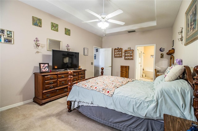 carpeted bedroom featuring a raised ceiling, connected bathroom, and ceiling fan