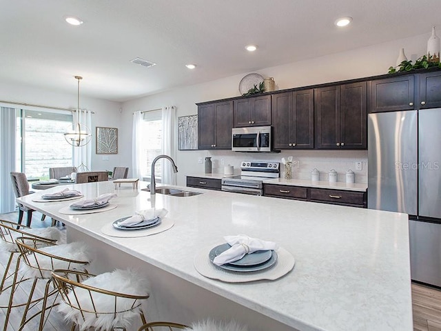 kitchen with appliances with stainless steel finishes, an island with sink, sink, hanging light fixtures, and dark brown cabinets