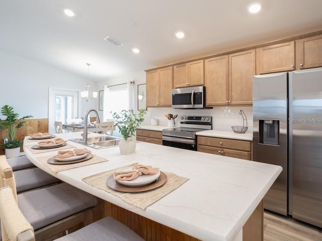 kitchen with stainless steel appliances, sink, a center island with sink, and decorative light fixtures