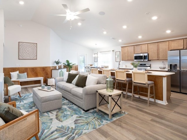 living room featuring vaulted ceiling, wooden walls, ceiling fan, and light wood-type flooring