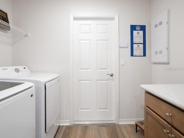 clothes washing area featuring cabinets, washing machine and dryer, and light hardwood / wood-style floors