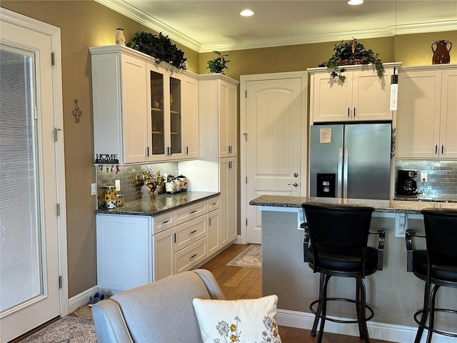 kitchen with stainless steel refrigerator with ice dispenser, white cabinetry, crown molding, dark stone counters, and hardwood / wood-style floors