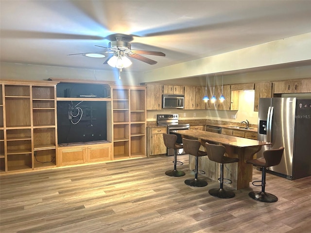 kitchen featuring sink, wood-type flooring, decorative light fixtures, appliances with stainless steel finishes, and a kitchen breakfast bar