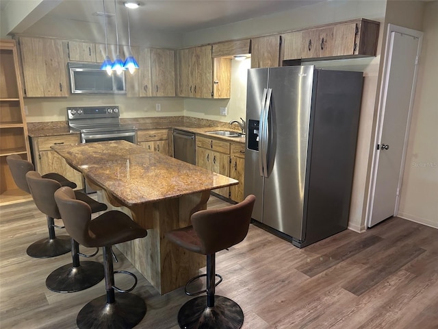 kitchen with pendant lighting, sink, appliances with stainless steel finishes, hardwood / wood-style floors, and light stone countertops