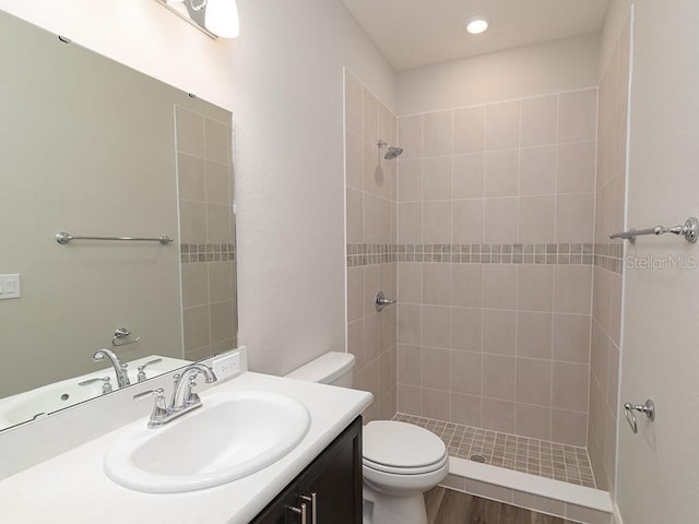 bathroom featuring hardwood / wood-style flooring, vanity, tiled shower, and toilet