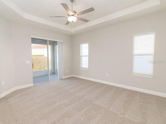 spare room with ceiling fan, a raised ceiling, and light carpet