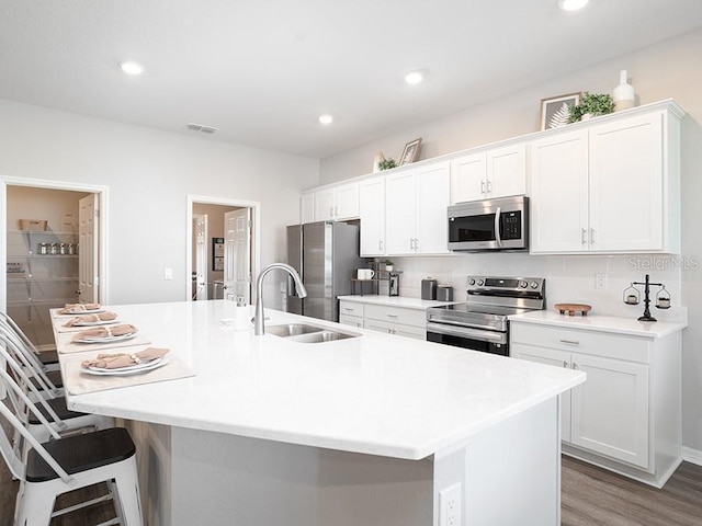 kitchen with stainless steel appliances, an island with sink, and white cabinets