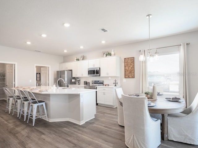 kitchen featuring stainless steel appliances, hanging light fixtures, a center island with sink, and white cabinets