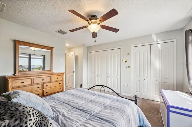 bedroom featuring ceiling fan, dark carpet, a textured ceiling, and two closets