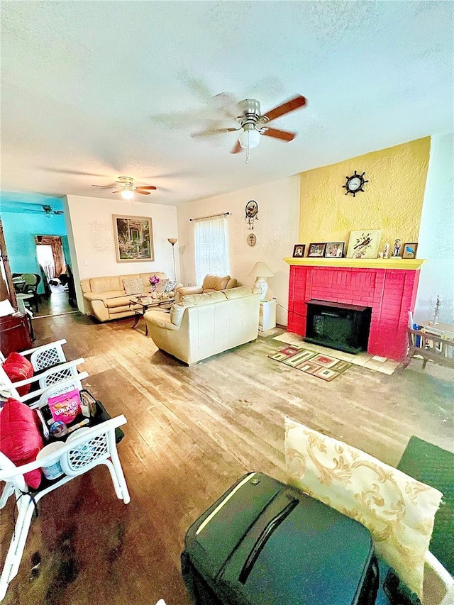 living room featuring ceiling fan, a brick fireplace, hardwood / wood-style floors, and a textured ceiling