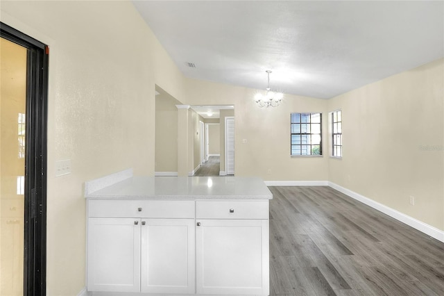 interior space with a notable chandelier, white cabinets, decorative light fixtures, vaulted ceiling, and light wood-type flooring