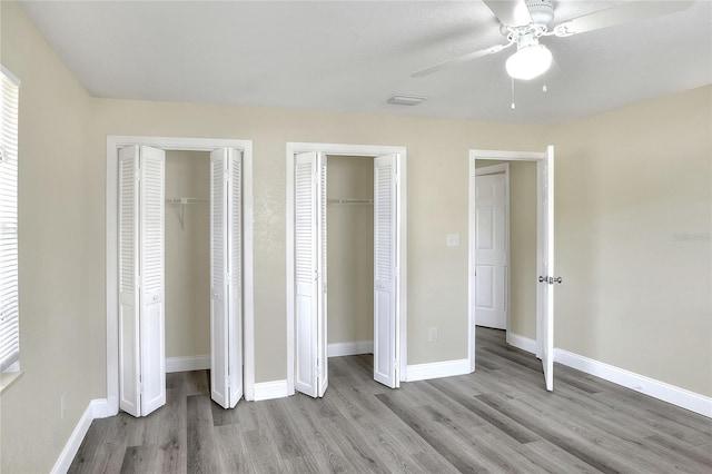 unfurnished bedroom featuring ceiling fan, light hardwood / wood-style flooring, and multiple closets