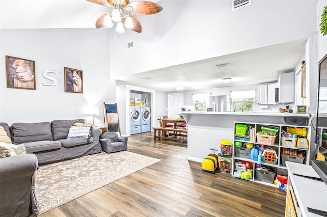 living room with vaulted ceiling, wood-type flooring, ceiling fan, washing machine and dryer, and a textured ceiling