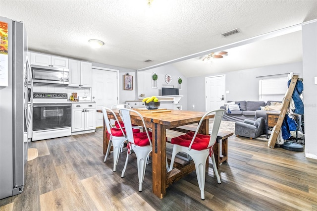 dining space featuring hardwood / wood-style floors, vaulted ceiling, and a textured ceiling