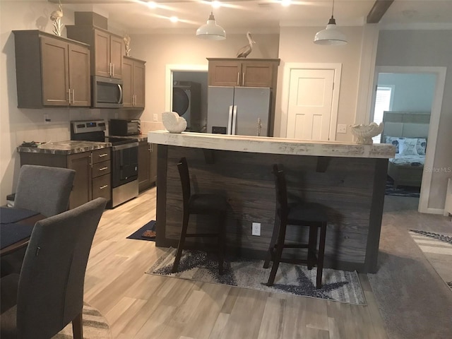 kitchen with hanging light fixtures, light hardwood / wood-style flooring, stainless steel appliances, and a kitchen bar