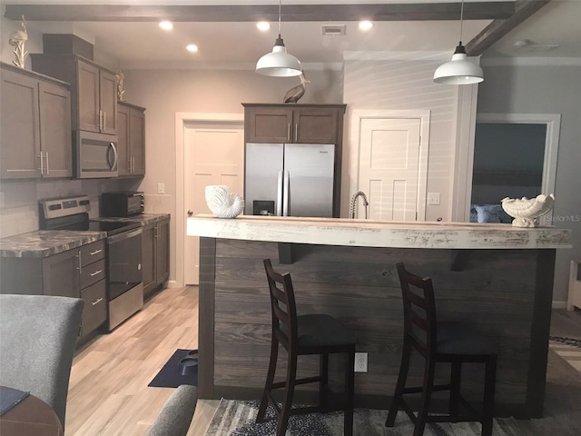 kitchen featuring appliances with stainless steel finishes, a breakfast bar, pendant lighting, tasteful backsplash, and light hardwood / wood-style flooring