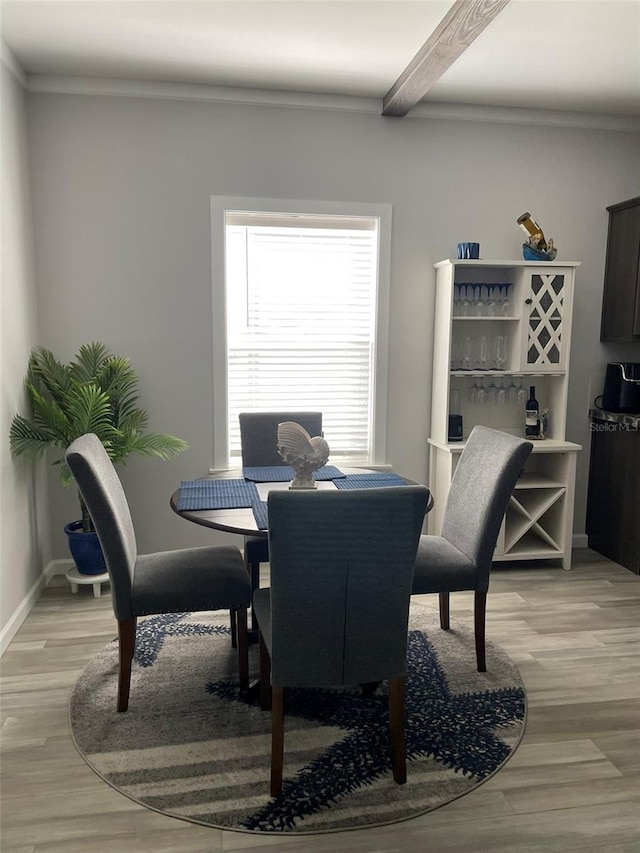 dining space with light wood-type flooring, baseboards, and beam ceiling