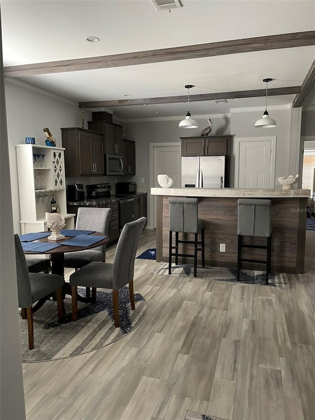 dining area featuring ornamental molding, light wood finished floors, beam ceiling, and visible vents