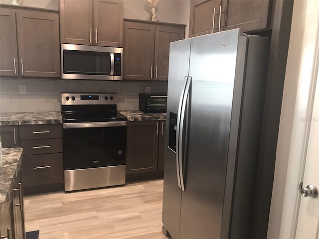 kitchen featuring dark stone countertops, dark brown cabinetry, stainless steel appliances, light wood-style flooring, and a toaster