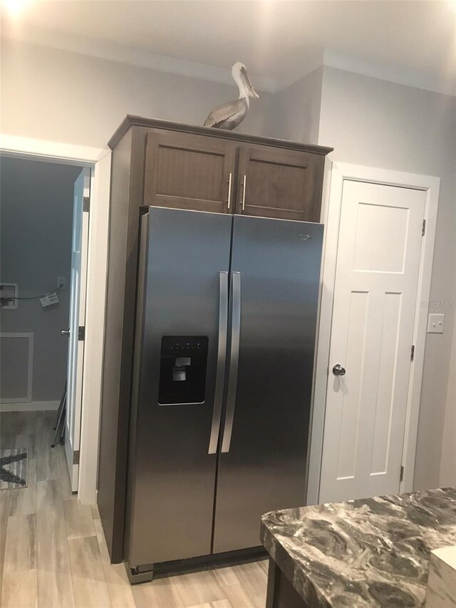 kitchen featuring stainless steel refrigerator with ice dispenser, light wood-type flooring, dark brown cabinets, and dark stone counters