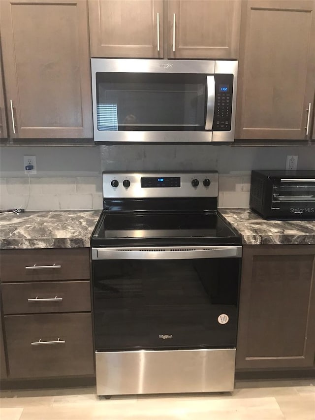 kitchen featuring dark brown cabinetry, a toaster, dark stone counters, and stainless steel appliances