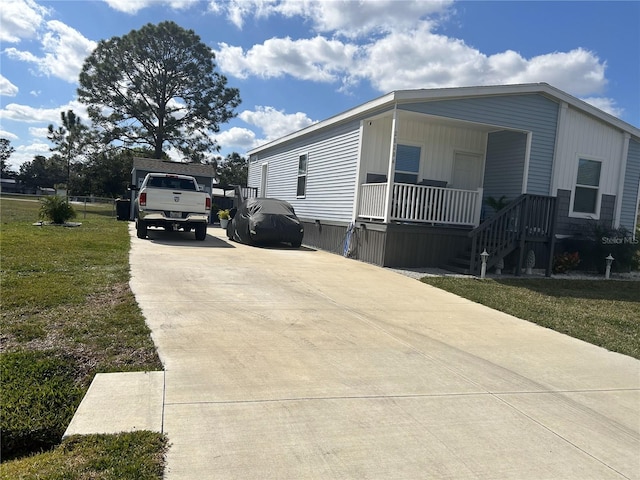 view of side of property featuring concrete driveway, a yard, and a porch