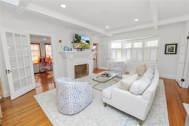 living room with plenty of natural light, beam ceiling, a brick fireplace, and light hardwood / wood-style flooring