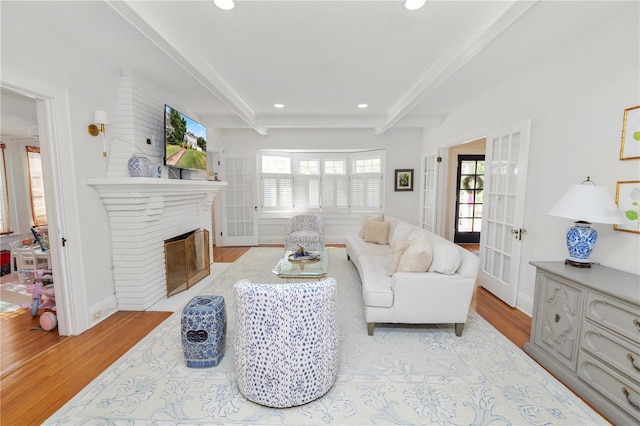 living room featuring french doors, a brick fireplace, beam ceiling, and light hardwood / wood-style flooring