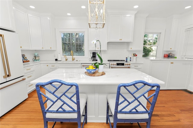 kitchen with decorative light fixtures, white cabinetry, high end white refrigerator, sink, and a kitchen breakfast bar