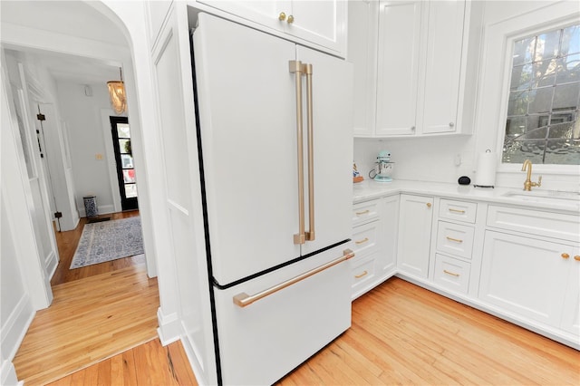 kitchen with white cabinetry, sink, high end white fridge, and light hardwood / wood-style flooring