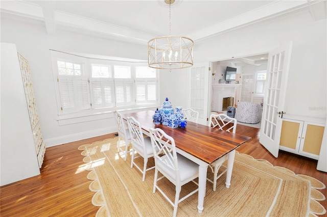 dining area with hardwood / wood-style floors, an inviting chandelier, a brick fireplace, beam ceiling, and french doors