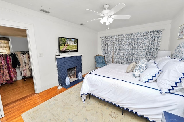 bedroom with crown molding, hardwood / wood-style flooring, a fireplace, and ceiling fan