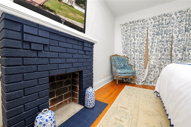 bedroom featuring a brick fireplace, wood-type flooring, and ornamental molding