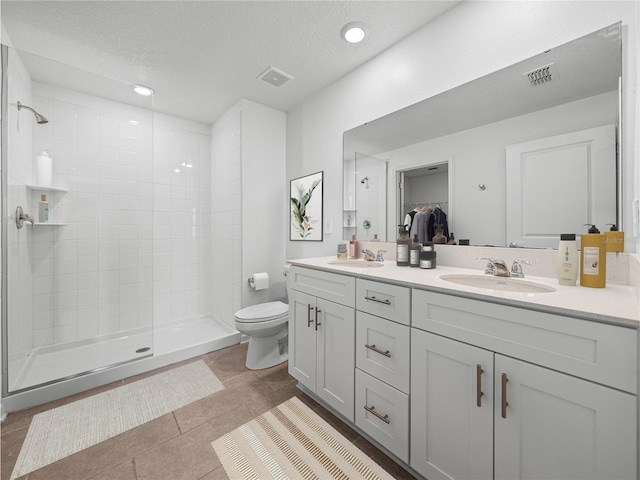 bathroom with tile patterned floors, toilet, a textured ceiling, a tile shower, and vanity