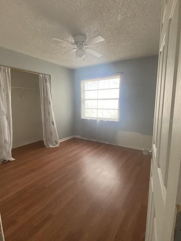 unfurnished bedroom featuring dark wood-type flooring, ceiling fan, a closet, and a textured ceiling