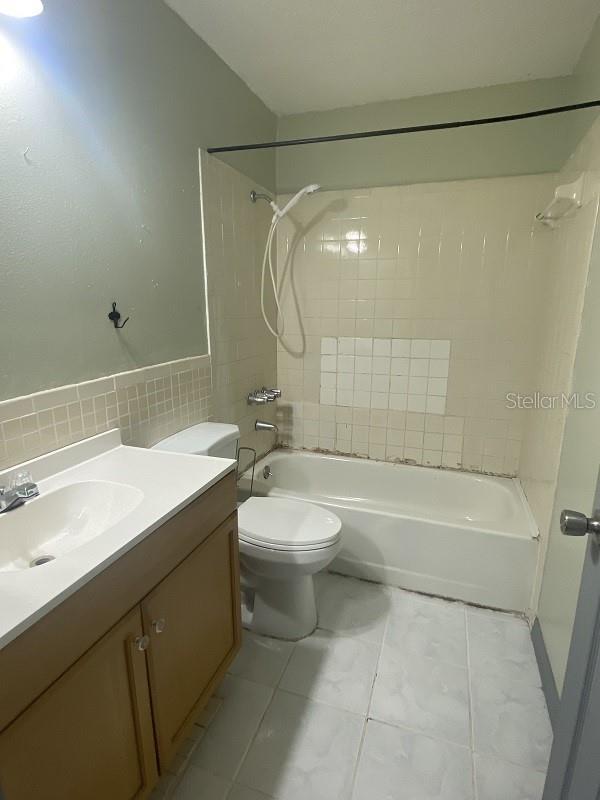 full bathroom with vanity, toilet, tiled shower / bath combo, and tile walls