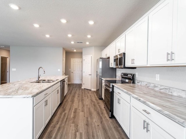 kitchen featuring appliances with stainless steel finishes, white cabinetry, sink, light stone counters, and a center island with sink