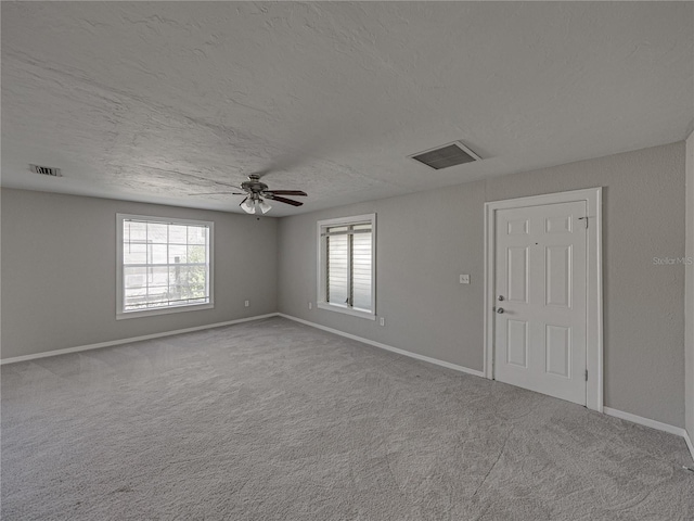 carpeted empty room with ceiling fan, plenty of natural light, and a textured ceiling