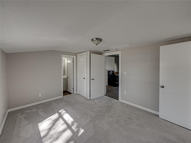 unfurnished bedroom featuring light colored carpet, lofted ceiling, and connected bathroom