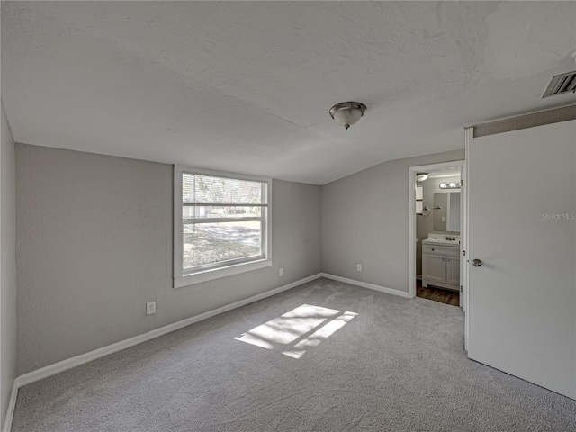 unfurnished bedroom with lofted ceiling, connected bathroom, light carpet, and a textured ceiling