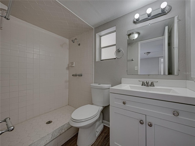 bathroom featuring wood-type flooring, tiled shower, vanity, and toilet