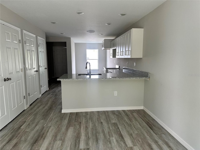 kitchen with sink, white cabinetry, dark hardwood / wood-style floors, kitchen peninsula, and light stone countertops