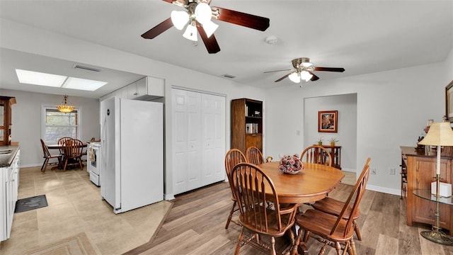 dining room featuring ceiling fan, a skylight, and light wood-type flooring