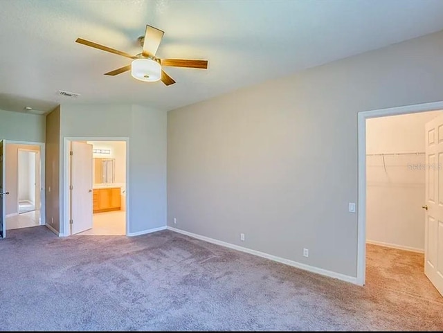 unfurnished bedroom featuring ensuite bath, a spacious closet, light colored carpet, a closet, and ceiling fan