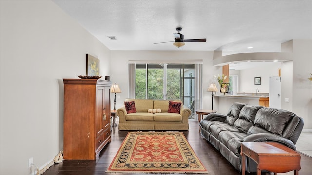 living room with dark wood finished floors, a ceiling fan, visible vents, and baseboards