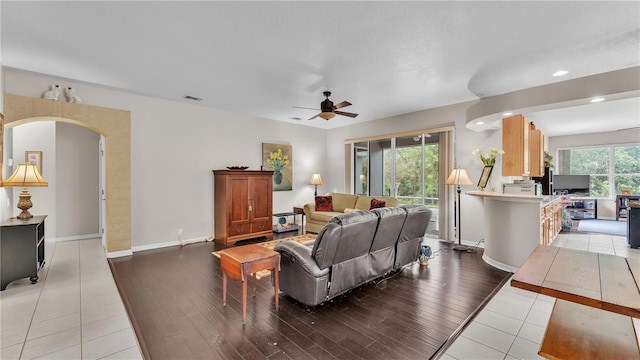 living room featuring a ceiling fan, light wood-style floors, visible vents, and arched walkways