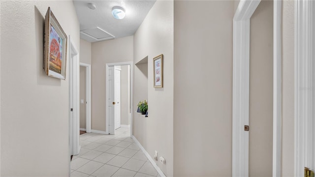 corridor featuring light tile patterned floors, baseboards, a textured ceiling, and attic access