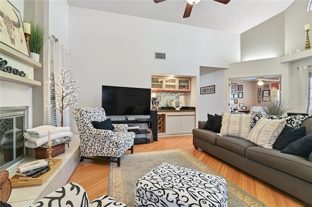 living room featuring ceiling fan, a towering ceiling, a textured ceiling, and light wood-type flooring